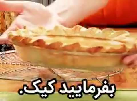 دستهایی یک پای میوهای خانگی را روی سینی جابهجا میکنند؛ متن میگوید بفرمایید کیک.