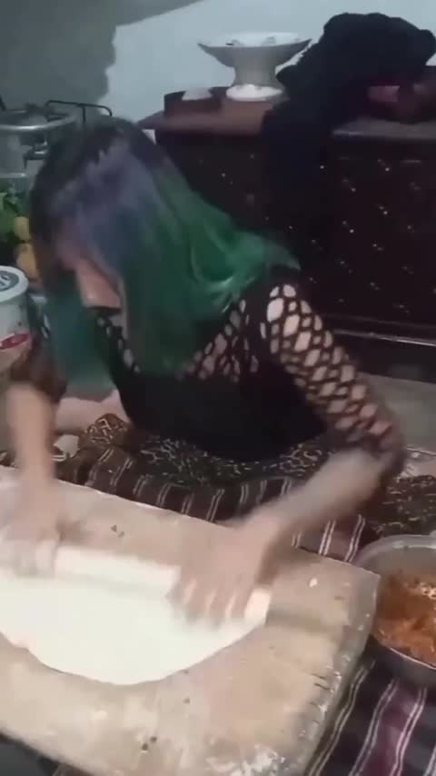 زنی با موهای سبز و آبی در آشپزخانه با وردنه خمیر نان پهن میکند و چهرهای اغراقشده دارد؛ متنی روی تصویر نیست.